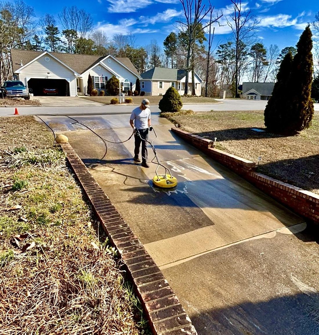 Concrete driveway being cleaned with a rotary surface cleaner, clean concrete behind the machine