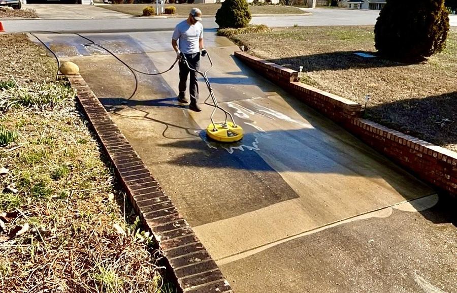 Rotary surface cleaner running across a concrete driveway in a residential neighborhood