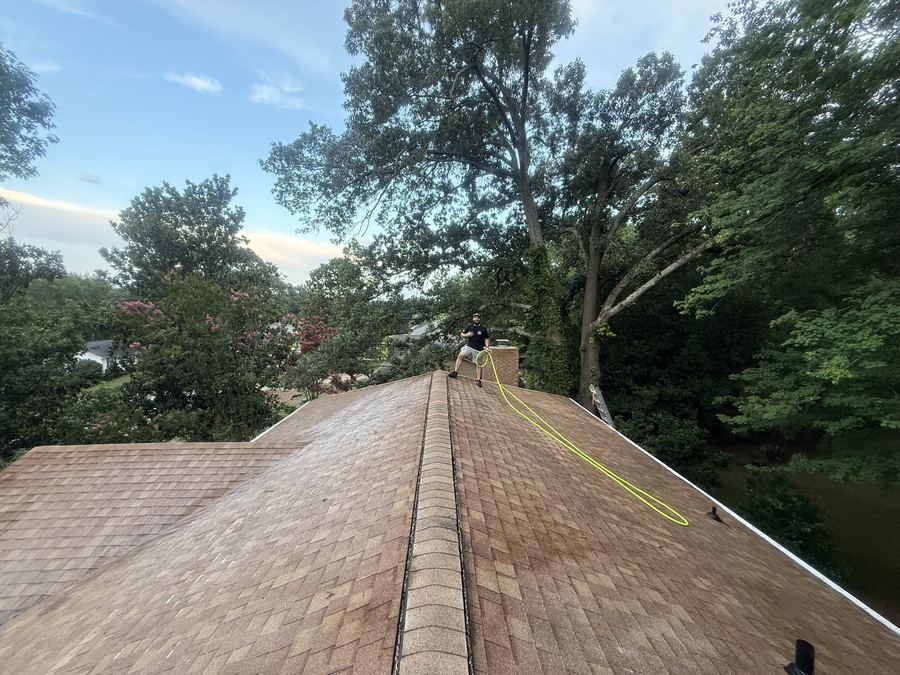 Roof ridge of a brown shingle roof being rinsed during a soft wash roof cleaning